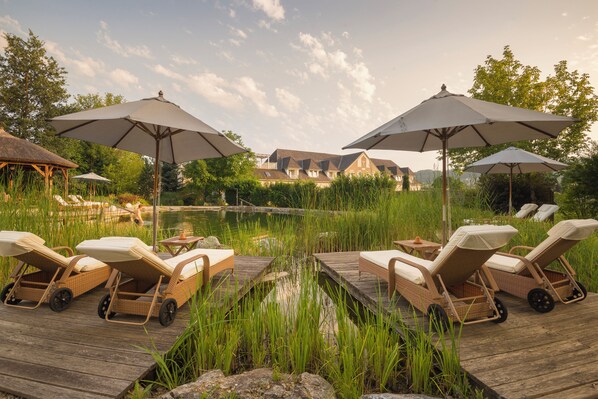 A lakeside deck with lounge chairs and umbrellas, a wooden dock, and a building in the background.