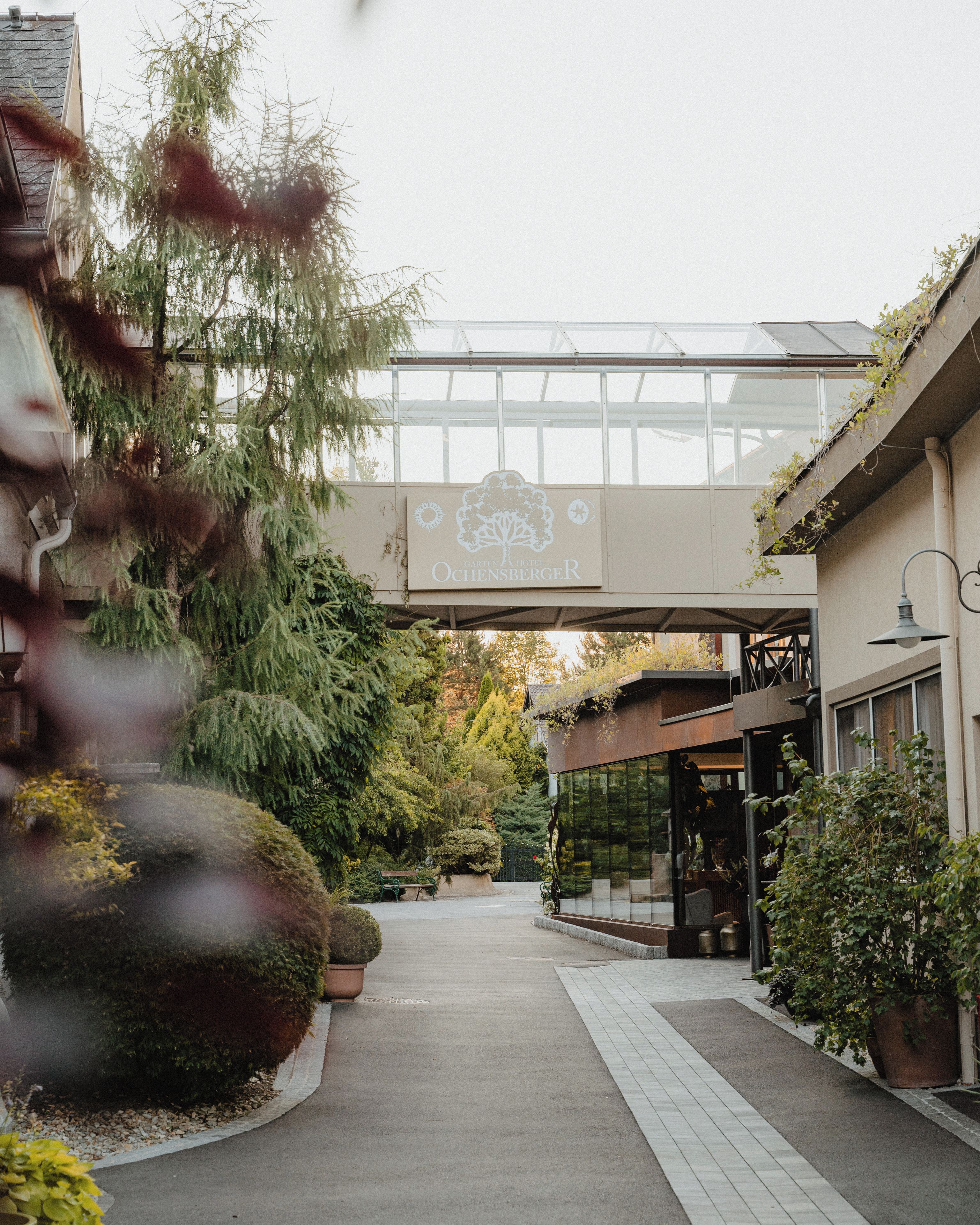 A hotel entrance with a glass canopy, potted plants, and a pathway leading to the building.