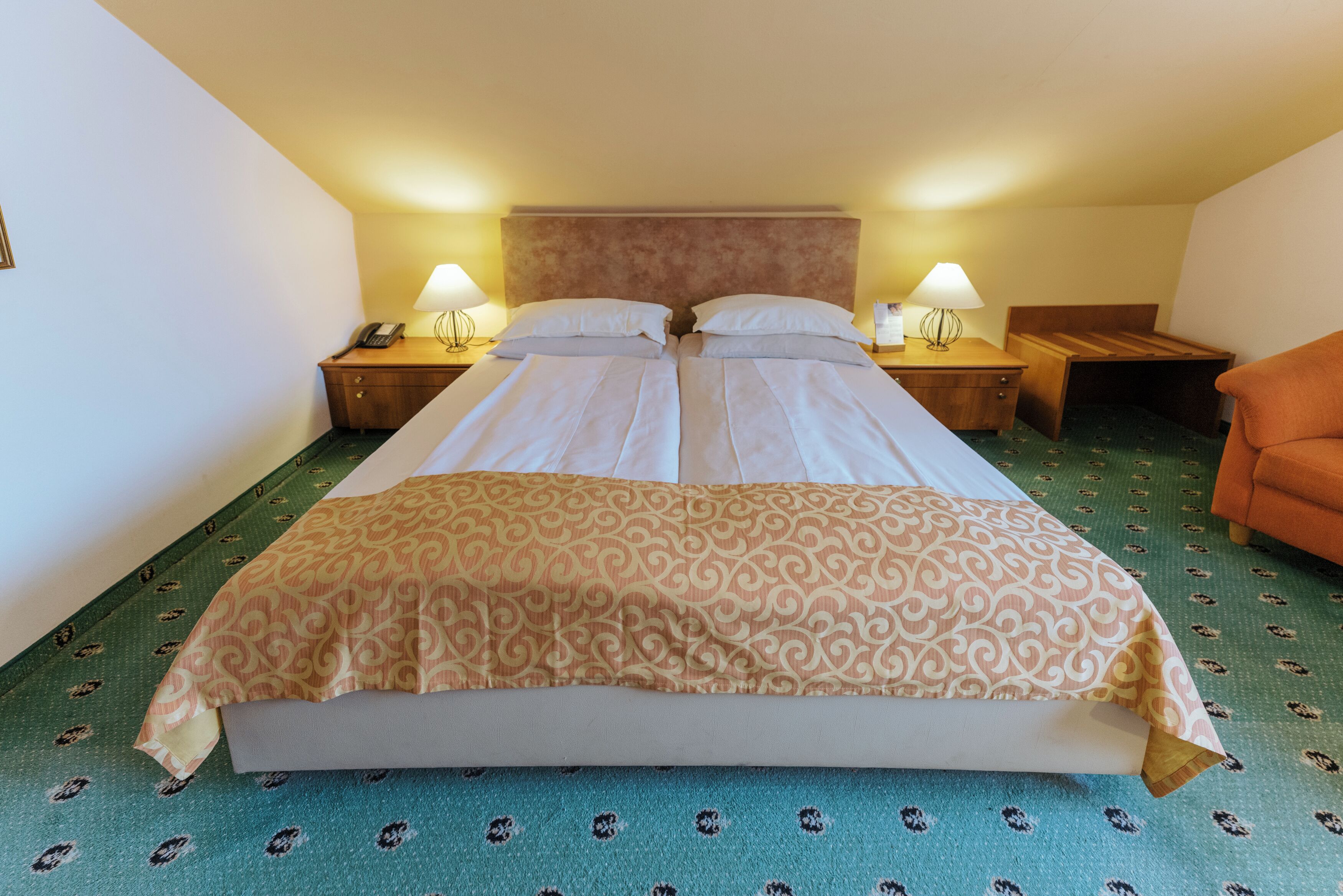 Una habitación de hotel con una cama grande, dos mesitas de noche con lámparas, un cabecero de madera y una alfombra estampada.