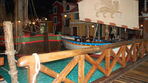 A model of a harbor with a wooden boat docked in a water channel, surrounded by model buildings and a wooden bridge. - Autohotel Venezia (Mirano)