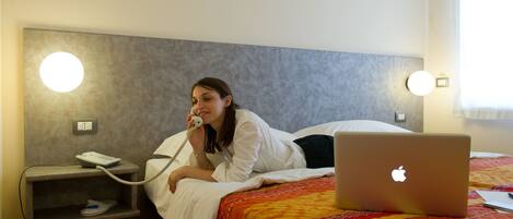 A hotel room with a bed, a bedside table with a phone, and a laptop on the bed.
