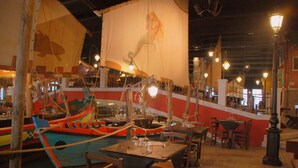 A restaurant with a nautical theme, featuring a large mural of a mermaid and a colorful boat. Tables are set with wine glasses and cutlery. - Autohotel Venezia (Mirano)