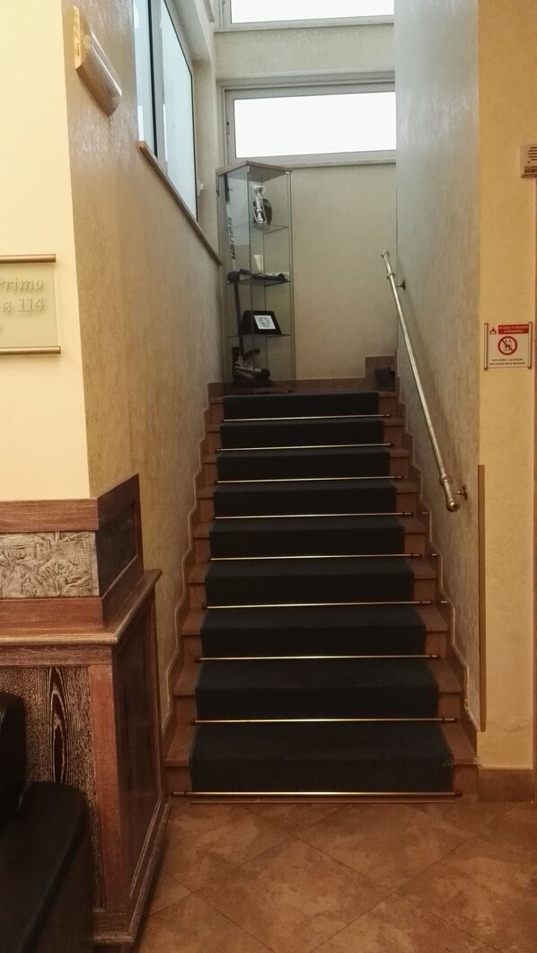 A staircase with black carpeted steps leading to a landing. - Borgo del Mare (Civitavecchia)