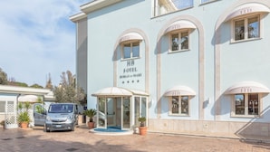 A light blue hotel with "HB HOTEL BORGO do MAR" signage, a covered entrance, and a parked van. - Borgo del Mare (Civitavecchia)