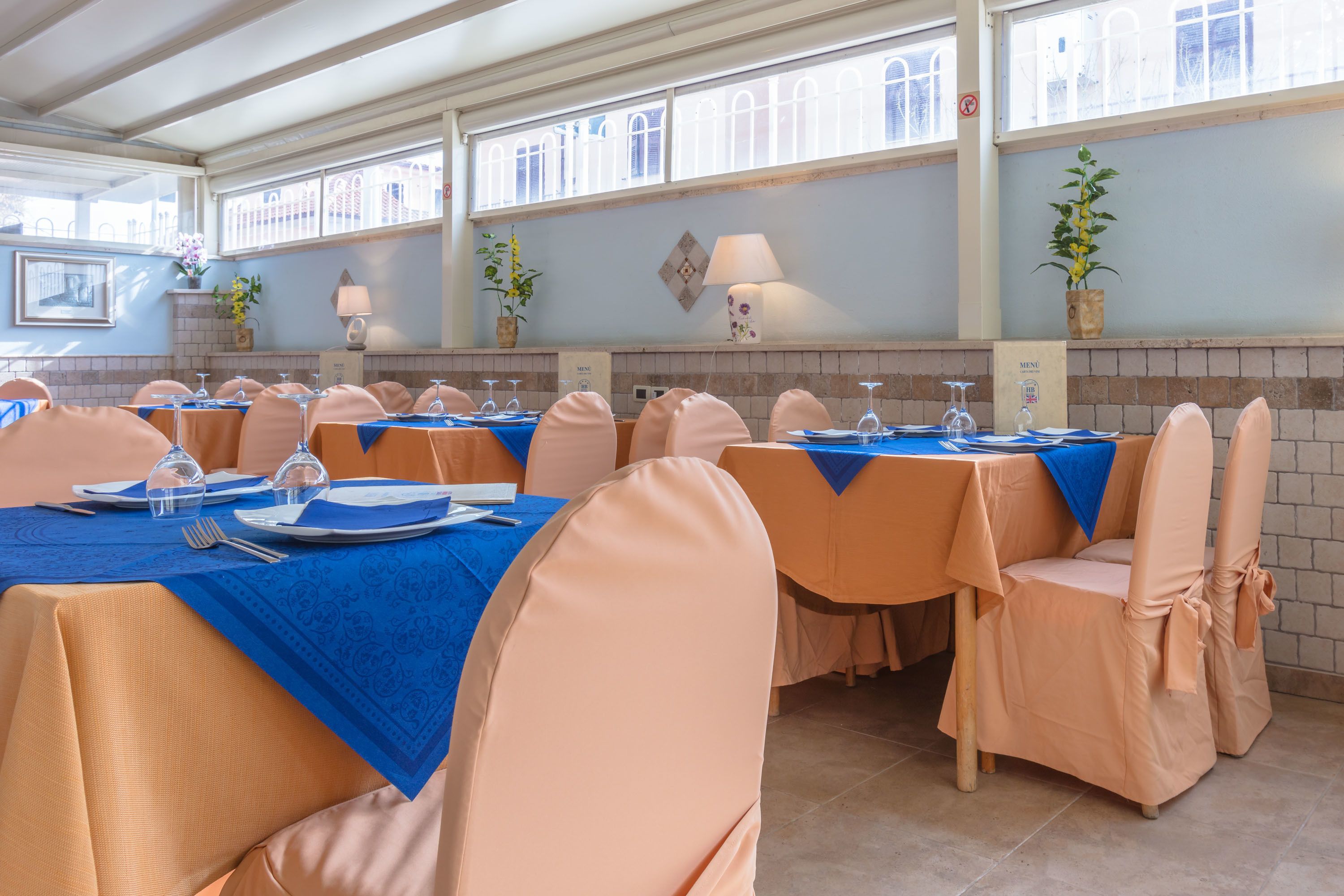 Un restaurant avec de nombreuses tables dressées pour le service, agrémenté de nappes bleues et de chaises de couleur pêche.