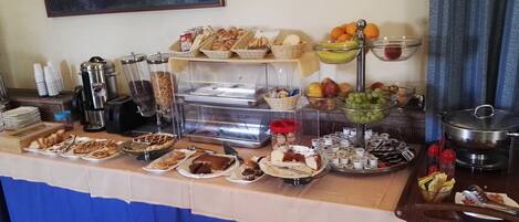 Une table de buffet proposant une variété d’aliments, notamment des pâtisseries, des fruits et des boissons.