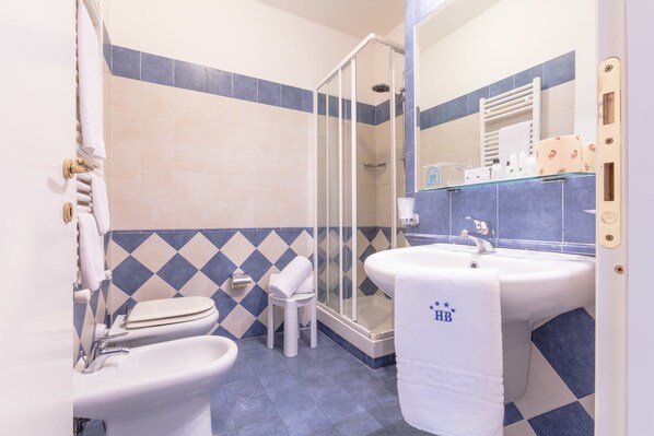 Une salle de bain comprenant des toilettes, un bidet, un lavabo et une douche.