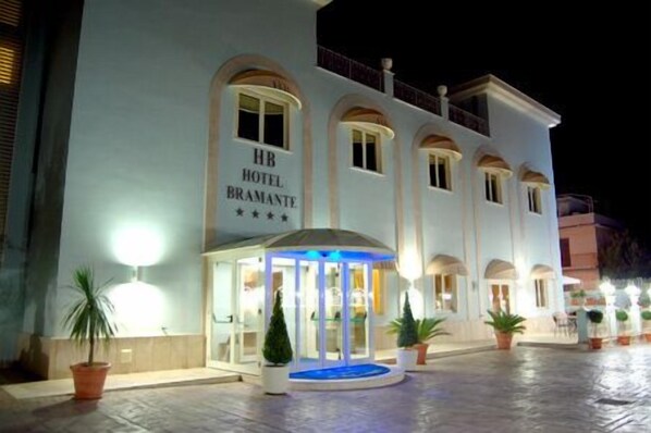 Un hotel con un letrero que dice "HB HOTEL BRAMANTE" y una entrada cubierta con una fuente iluminada en azul.