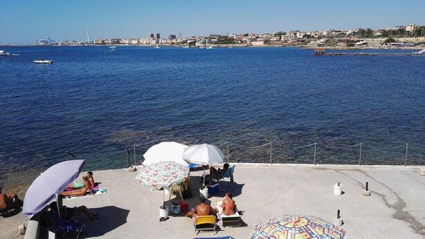 A seaside view with a pier, people relaxing under umbrellas, and boats on the water. - Borgo del Mare (Civitavecchia)