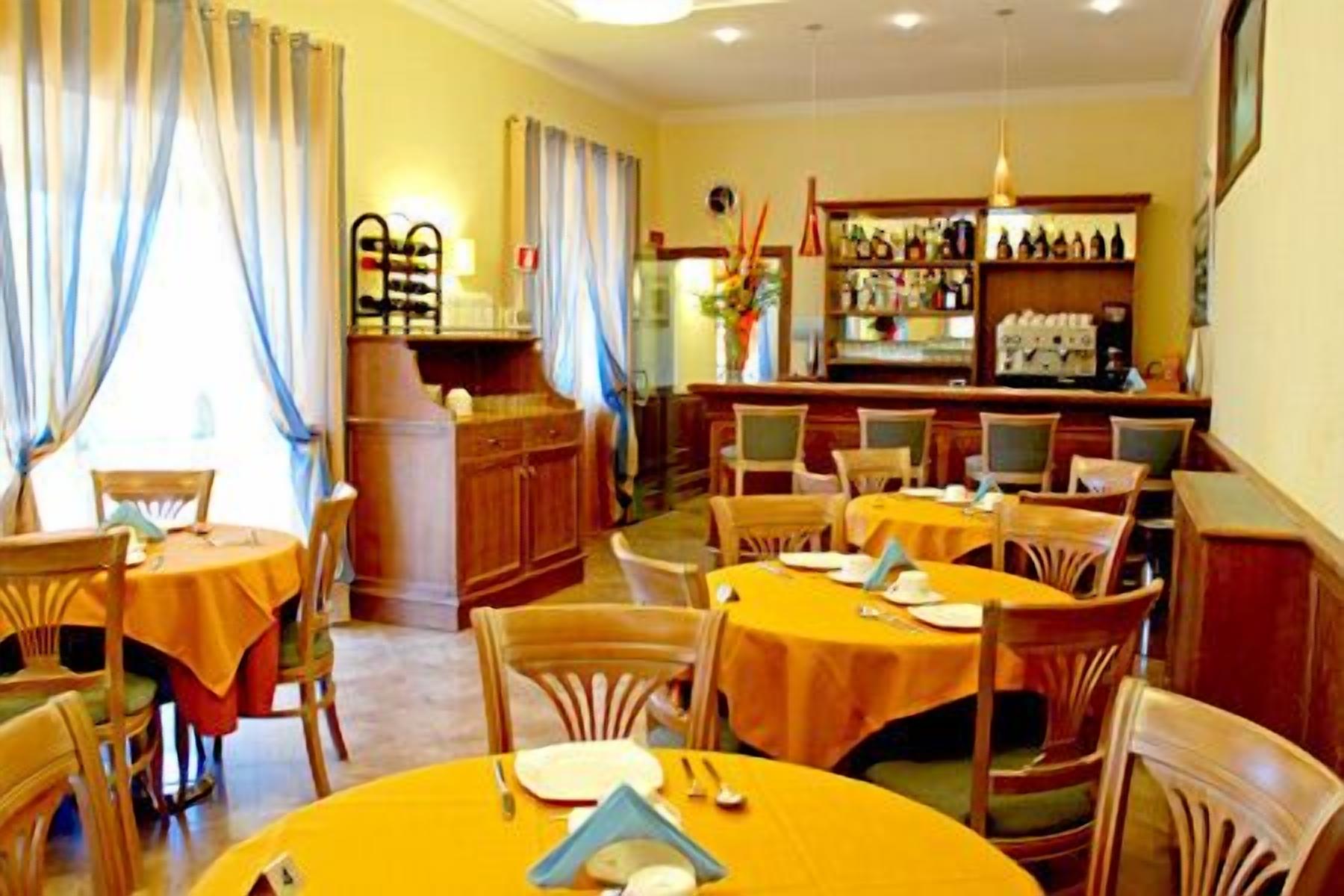 Un restaurant avec des tables et des chaises rondes, un bar avec des étagères remplies de bouteilles et des rideaux aux fenêtres.