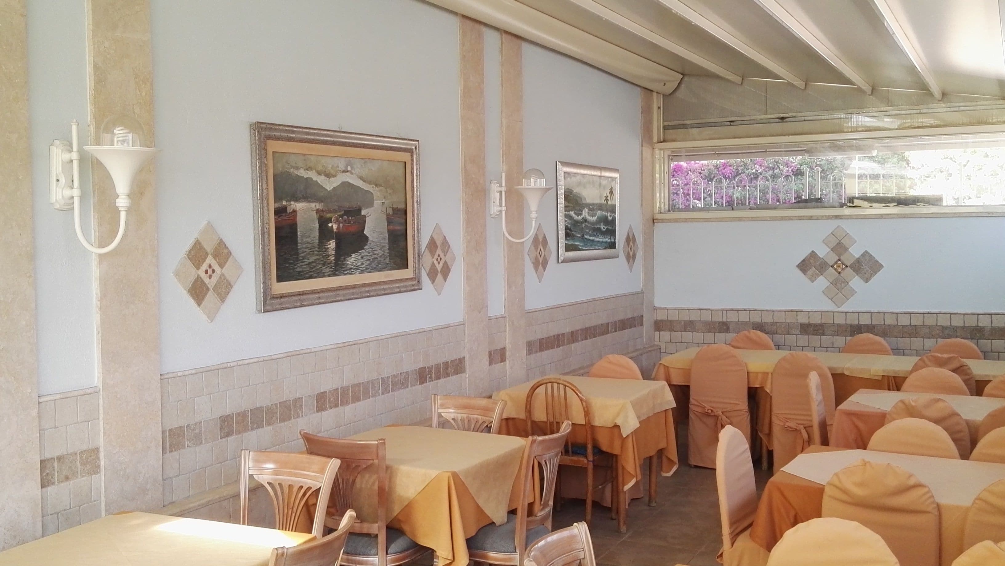Un ristorante con diversi tavoli e sedie, quadri appesi alle pareti e uno schienale piastrellato.