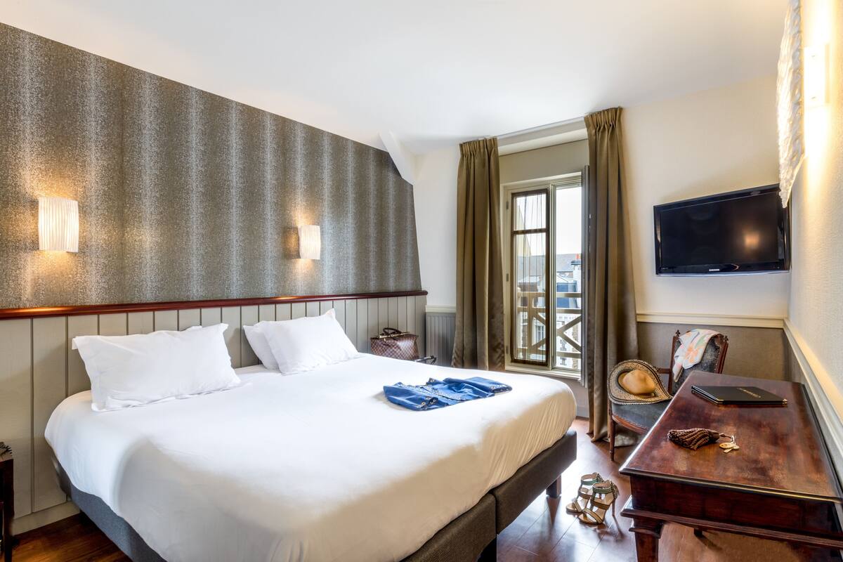 Ein Hotelzimmer mit einem großen Bett, einem Schreibtisch, einem Fernseher und Blick auf die Stadt.