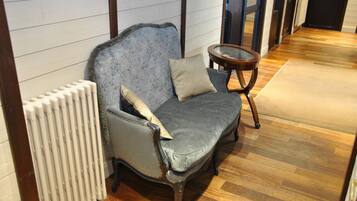 A grey upholstered sofa with a cushion, positioned next to a radiator and a small round wooden table.