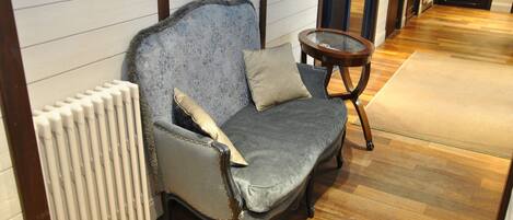 A grey upholstered sofa with a cushion, positioned next to a radiator and a small round wooden table.