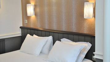 Een net opgemaakt bed met witte lakens en kussens, een houten hoofdbord en twee wandlampen op een structuurwand.