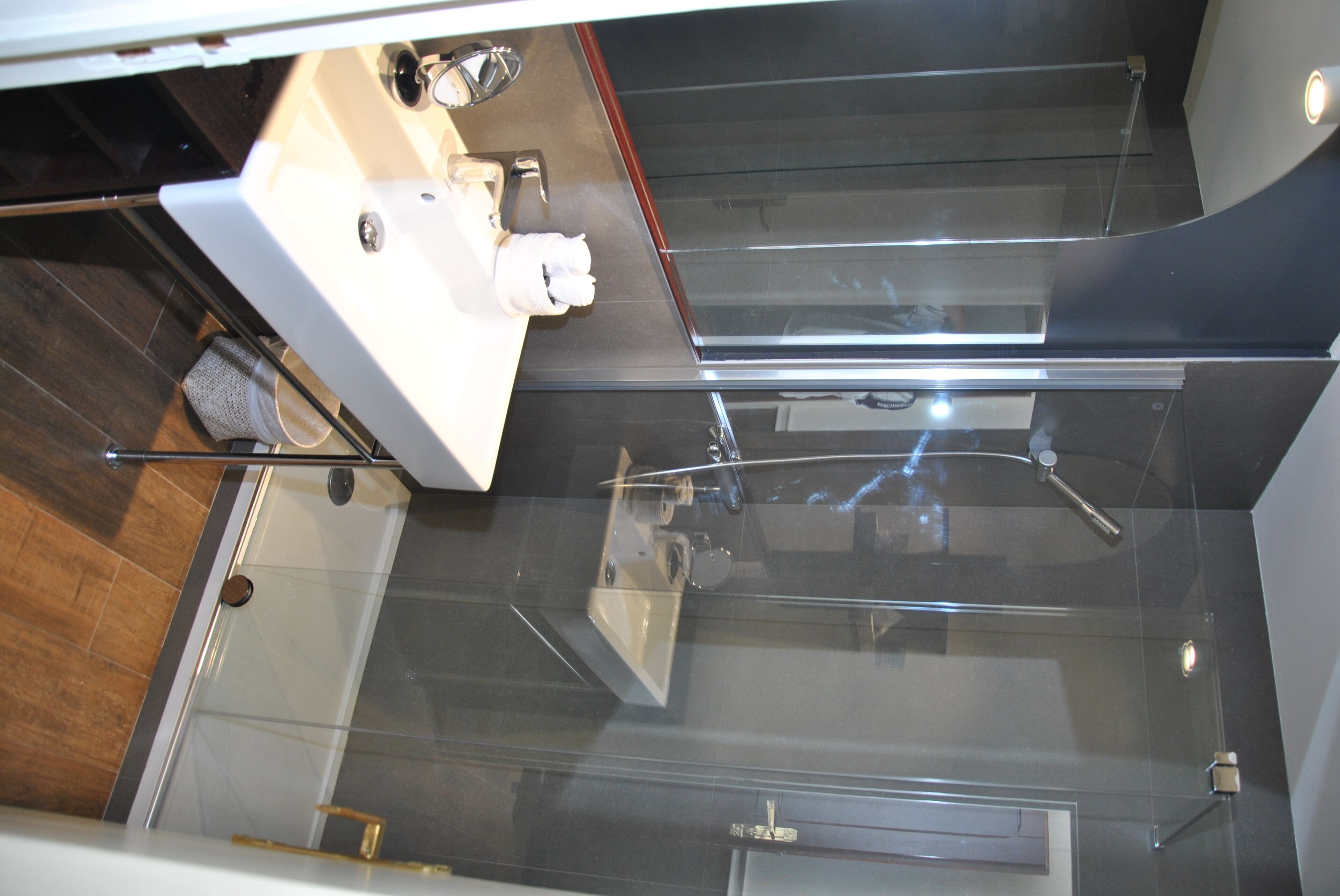 A modern bathroom with a glass shower enclosure, a white sink with a mirror, and a towel rack.