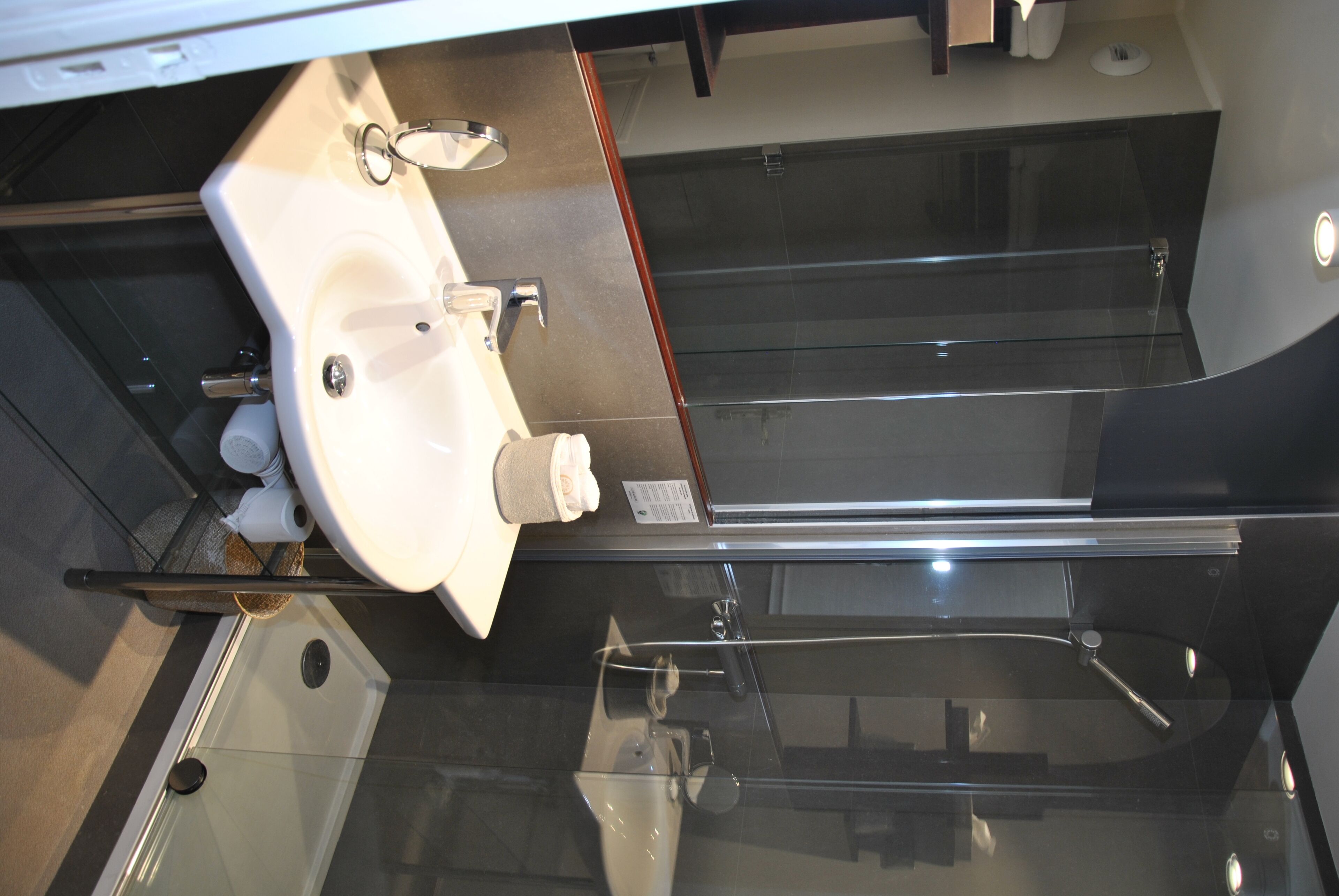 Een moderne badkamer met een douchecabine van glas, een witte wastafel en een roestvrijstalen kraan.