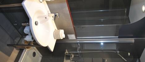 Een moderne badkamer met een douchecabine van glas, een witte wastafel en een roestvrijstalen kraan.