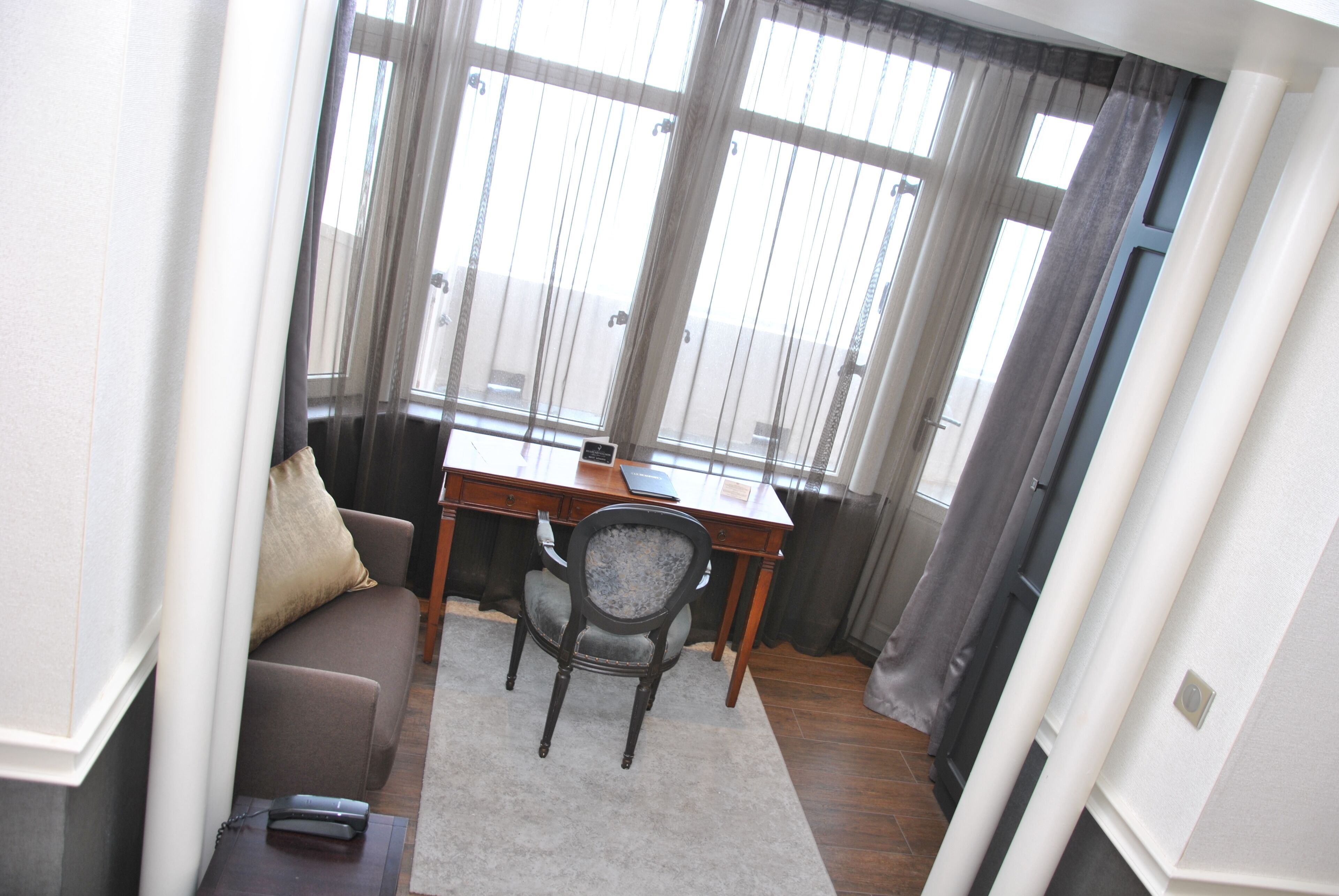 A small, well-lit room with a wooden desk, a cushioned chair, and a sofa.