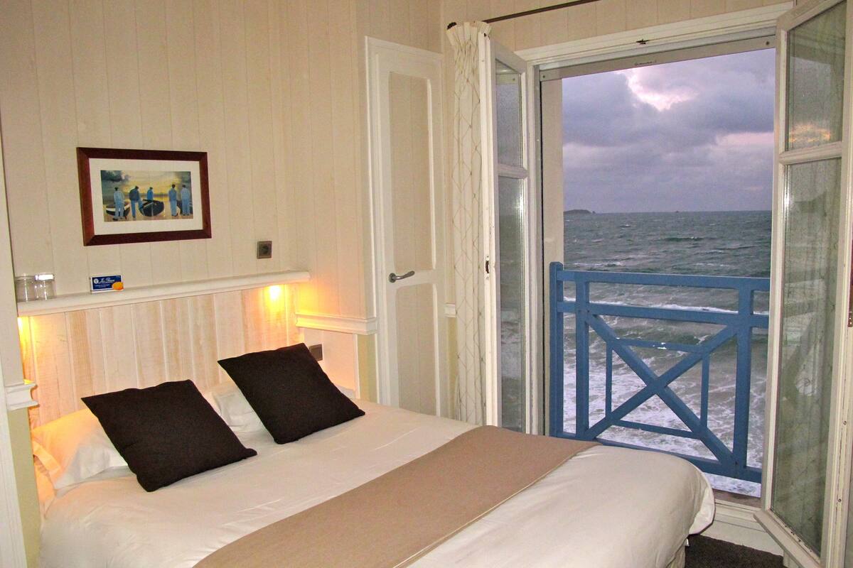 Ein Schlafzimmer mit einem Bett und einer Tür, die auf einen Balkon mit Meerblick führt.
