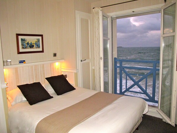 Een slaapkamer met een bed en een deur naar een balkon met uitzicht op zee.
