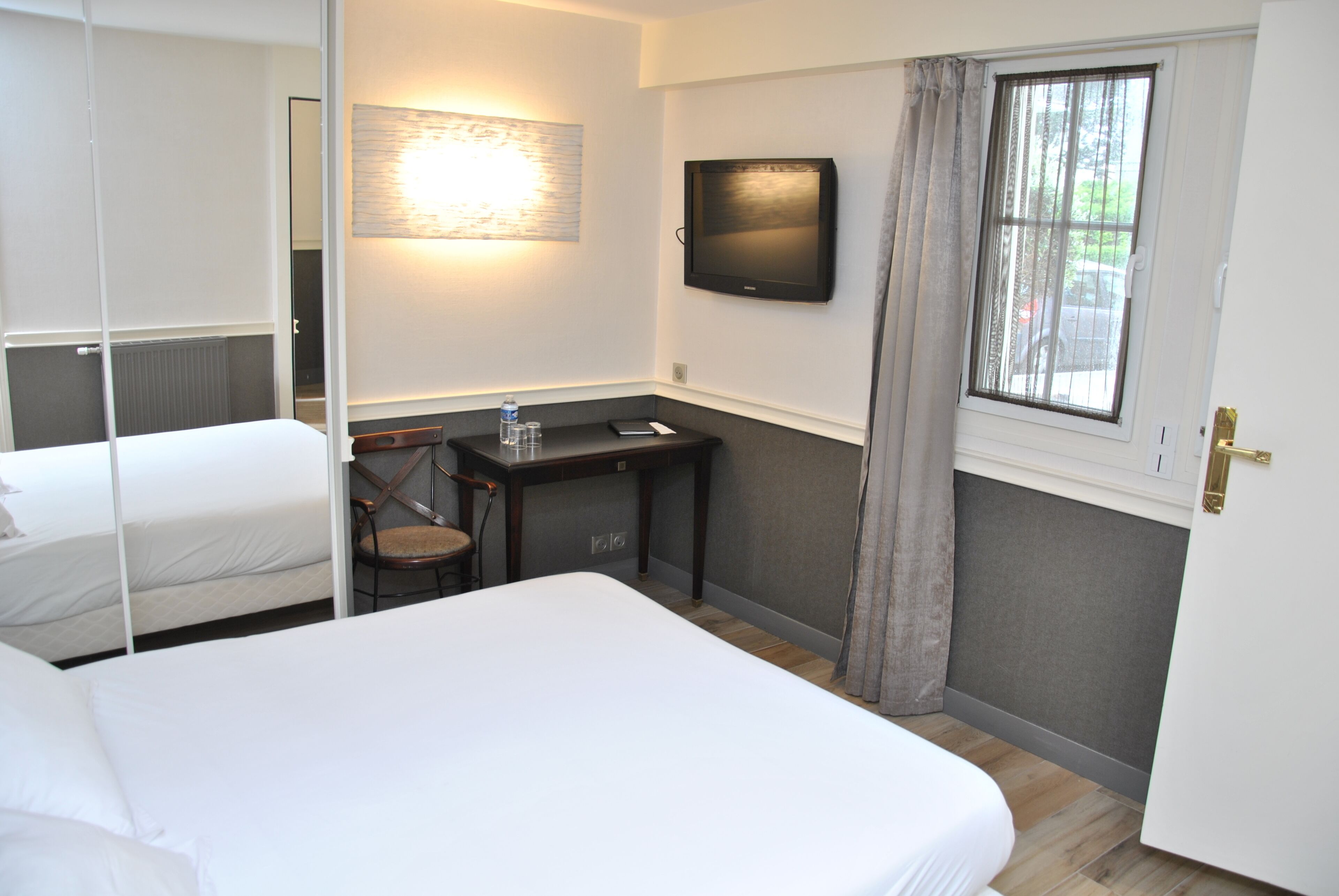 Ett hotellrum med en säng, ett skrivbord, en stol, en tv och ett fönster med gardiner.