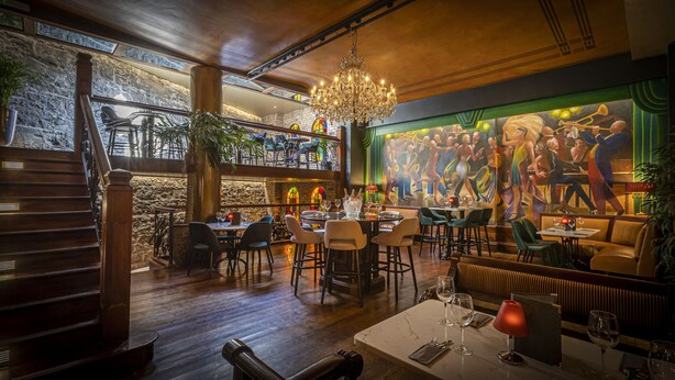 A restaurant with a chandelier, wooden staircase, and a mural of dancers. - Victoria Hotel (Galway)