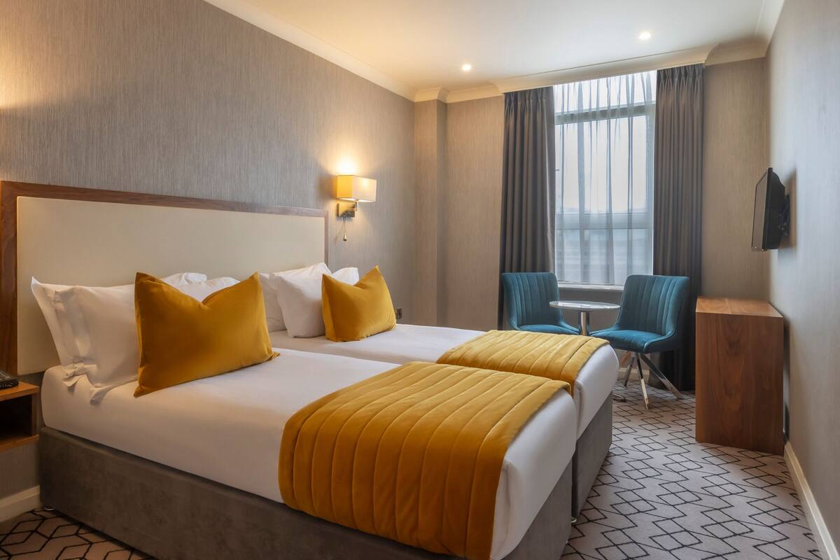 Une chambre d’hôtel avec deux lits, un bureau, une chaise et un téléviseur.