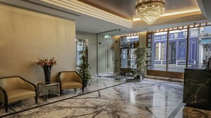 A lobby with marble flooring, two sofas, a chandelier, and a large window with a view of a building. - Eyre Square Hotel (Galway)