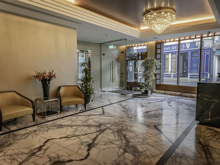 Um hall de entrada com piso de mármore, dois sofás, um candelabro e uma janela grande com vista para um edifício.