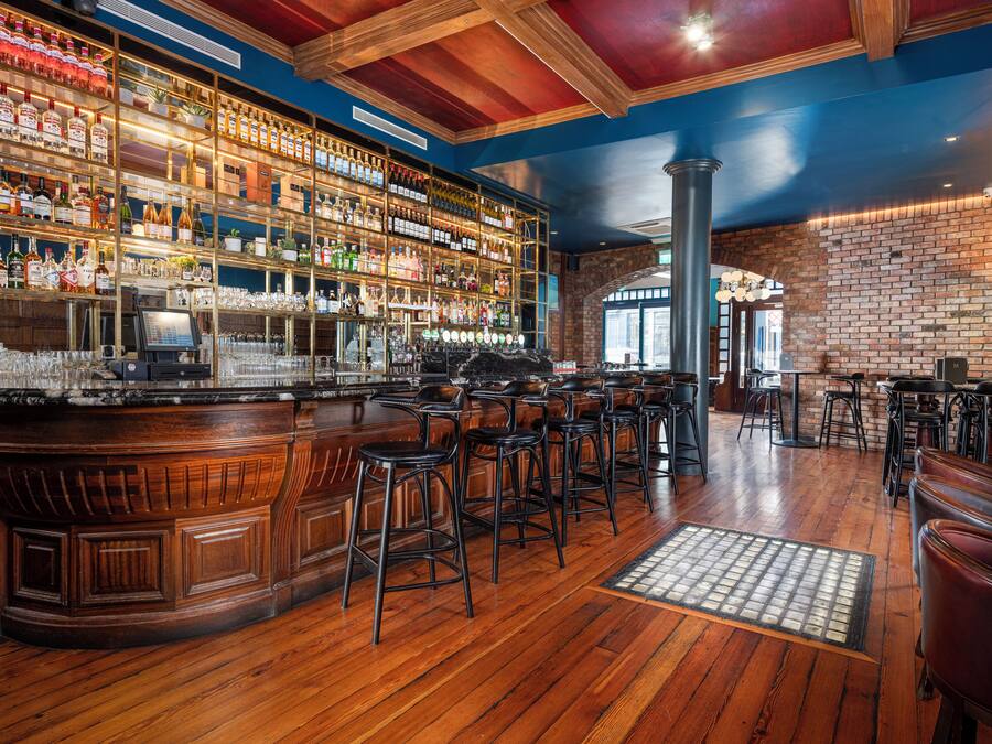 Um bar com piso de madeira, parede de tijolos e diversas garrafas e copos nas prateleiras.