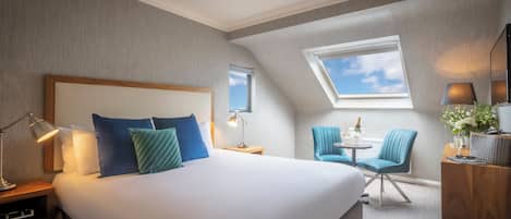 Hotelkamer met een groot bed, dakraam, een klein tafeltje met stoelen en een nachtkastje met lamp.