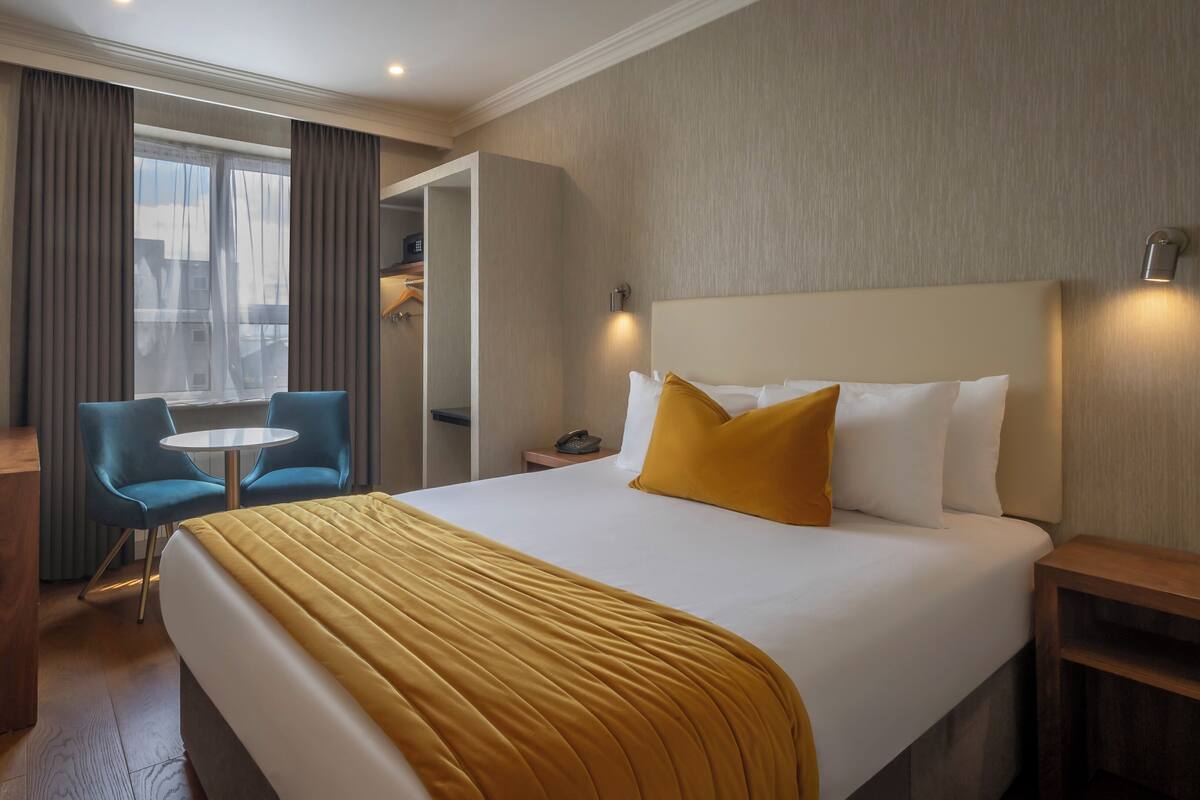 Una habitación de hotel con cama, escritorio, silla, una mesita y televisor.