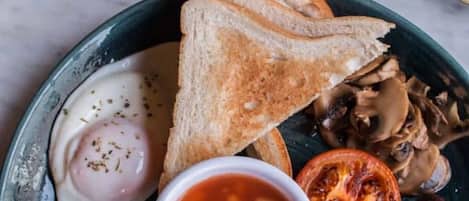 Un plato de desayuno con huevos benedictinos, tostadas, frijoles, tocino, champiñones, salchichas y tomate.