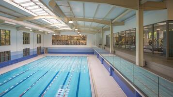 A large indoor swimming pool with multiple lanes, a high ceiling with skylights, and a glass wall on one side.