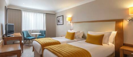 A hotel room with two beds, a desk, a chair, a TV, and a window with curtains.