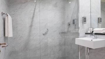 Un baño moderno con ducha de vidrio, lavamanos blanco y un espejo grande.