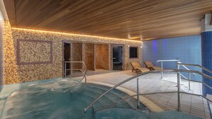 Un área de spa con piscina, techo de madera, paredes con azulejos y sillones de descanso.