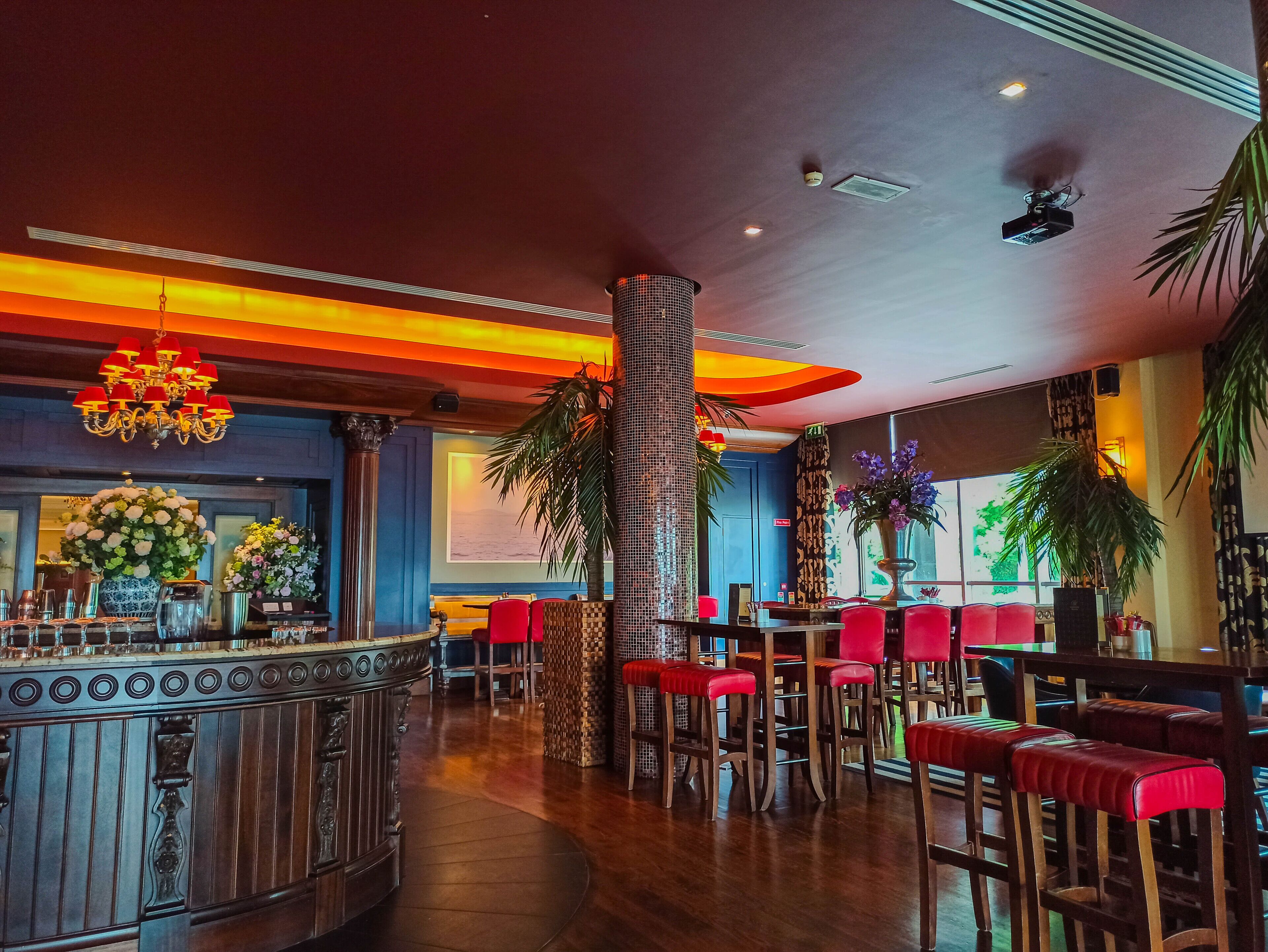 Una zona de bar con mostrador, taburetes rojos y una columna decorativa.