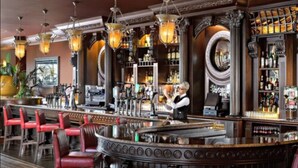 Un bar con sillas rojas, un camarero y una estantería repleta de licores.