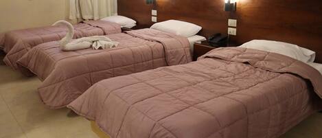 Een hotelkamer met drie bedden, elk voorzien van een roze sprei en witte kussens. Boven de bedden hangen wandlampen en op het nachtkastje staat een telefoon.