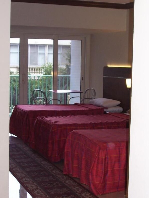 Quarto com duas camas, uma mesa e cadeiras, e uma varanda visível pela janela.