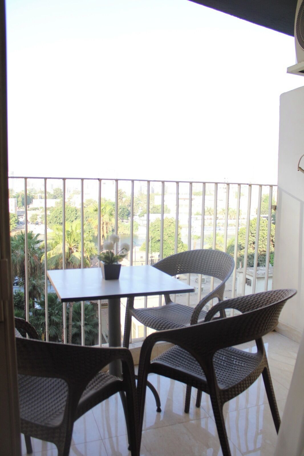 A balcony with a table and chairs, offering a view of a residential area with greenery and buildings.