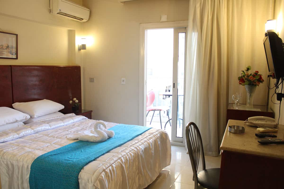 Ein Hotelzimmer mit Bett, Schreibtisch mit Telefon, Stuhl und Blick ins Freie durch eine Tür.