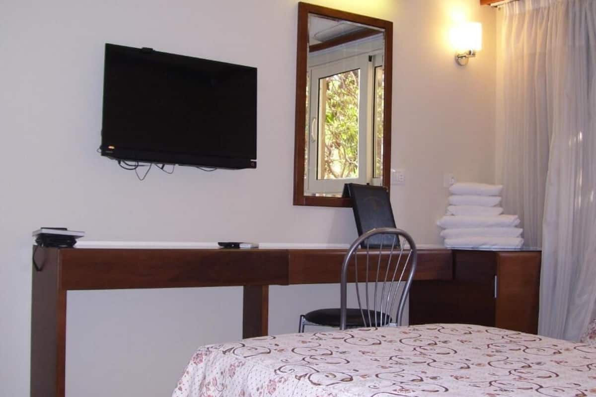 Ein Zimmer mit einem Bett, einem Schreibtisch, einem Stuhl, einem Fernseher, einem Spiegel und einem Fenster mit Vorhängen.