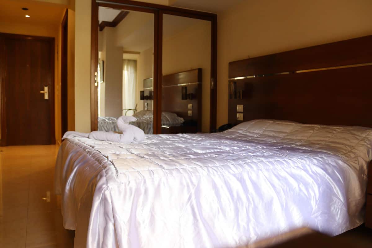 Ein Hotelzimmer mit einem großen Bett, einem Holzkopfstück, einem Spiegel in voller Größe und einer Tür zu einem anderen Raum.