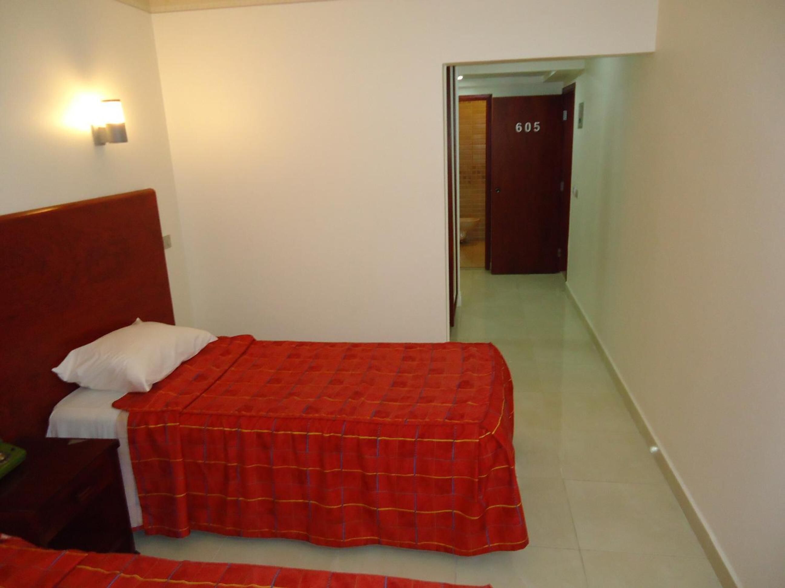 A small, clean room with a single bed, a nightstand, and a wall-mounted light.