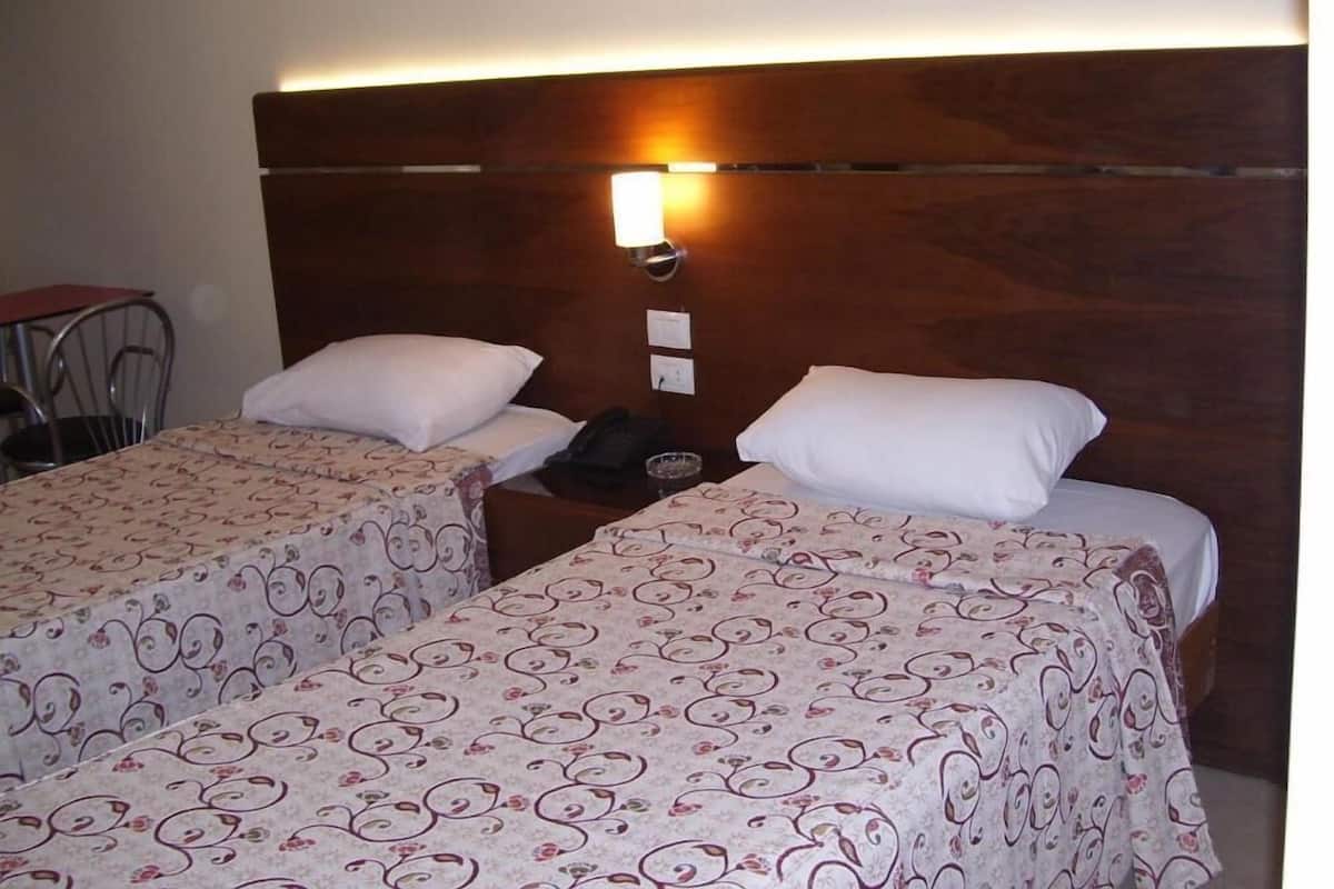 Ein Hotelzimmer mit zwei Betten, jeweils mit einem blumigen Überwurf, einem Holzkopfbrett und einer an der Wand montierten Lampe.