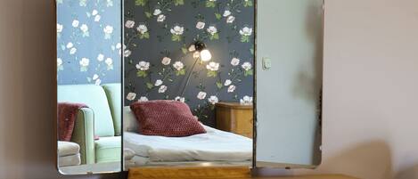 A wooden desk with a mirror, a green cushioned bench, and a floral wallpaper.