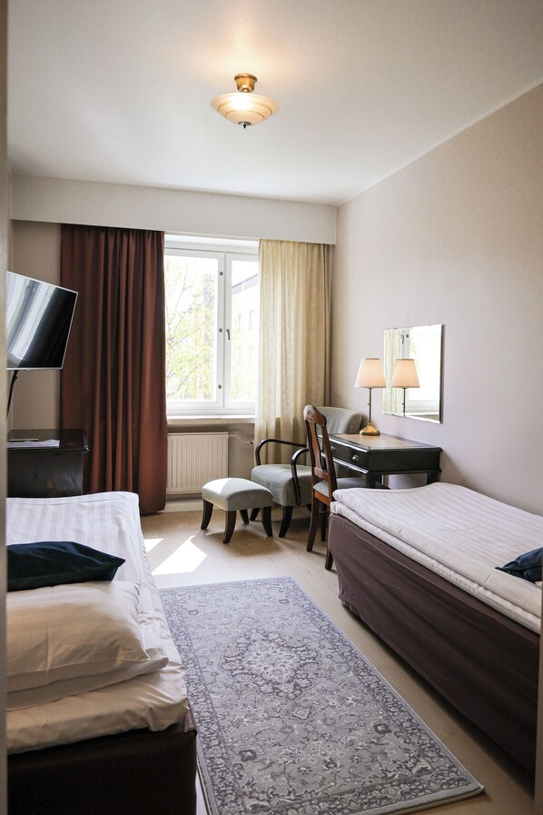 Habitación de hotel con dos camas, un escritorio, una silla, un televisor y una ventana con cortinas.